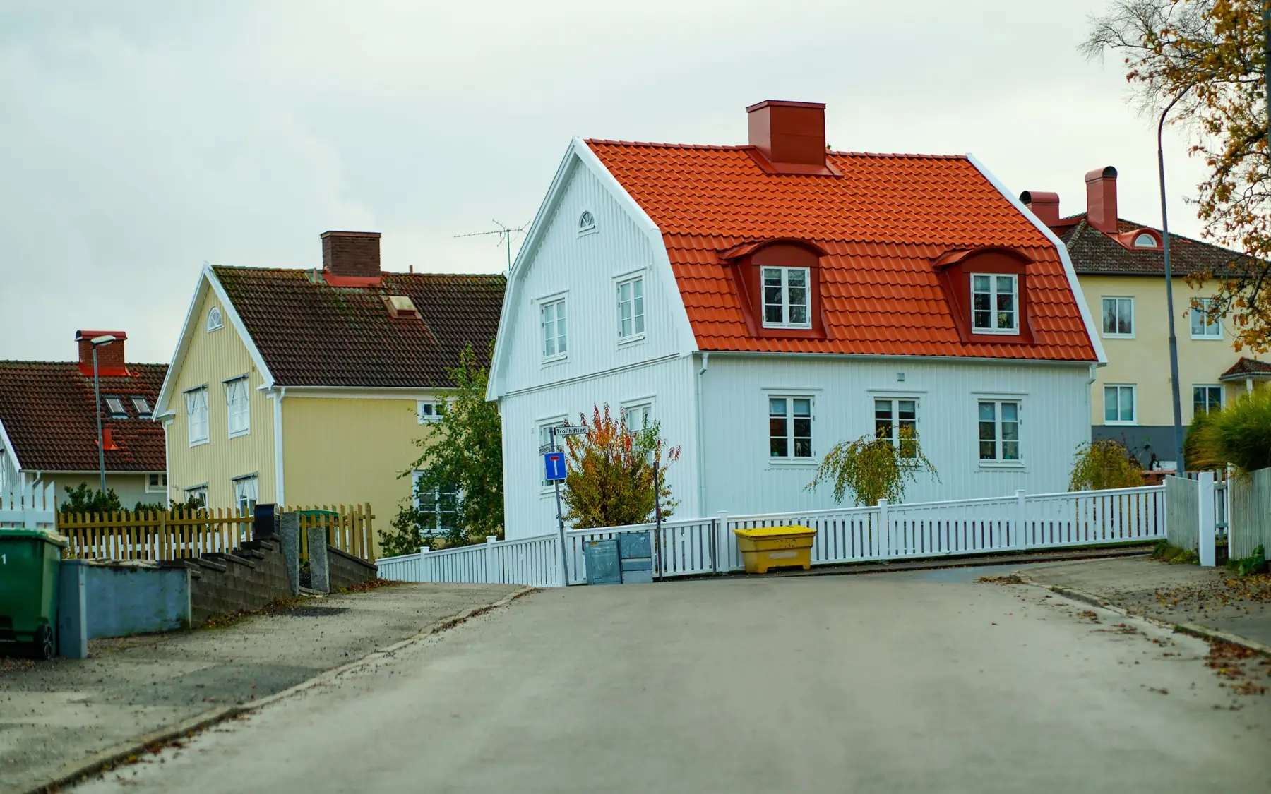 Lyseblått hus med rødt tak og hvitt stakitt i en villagate