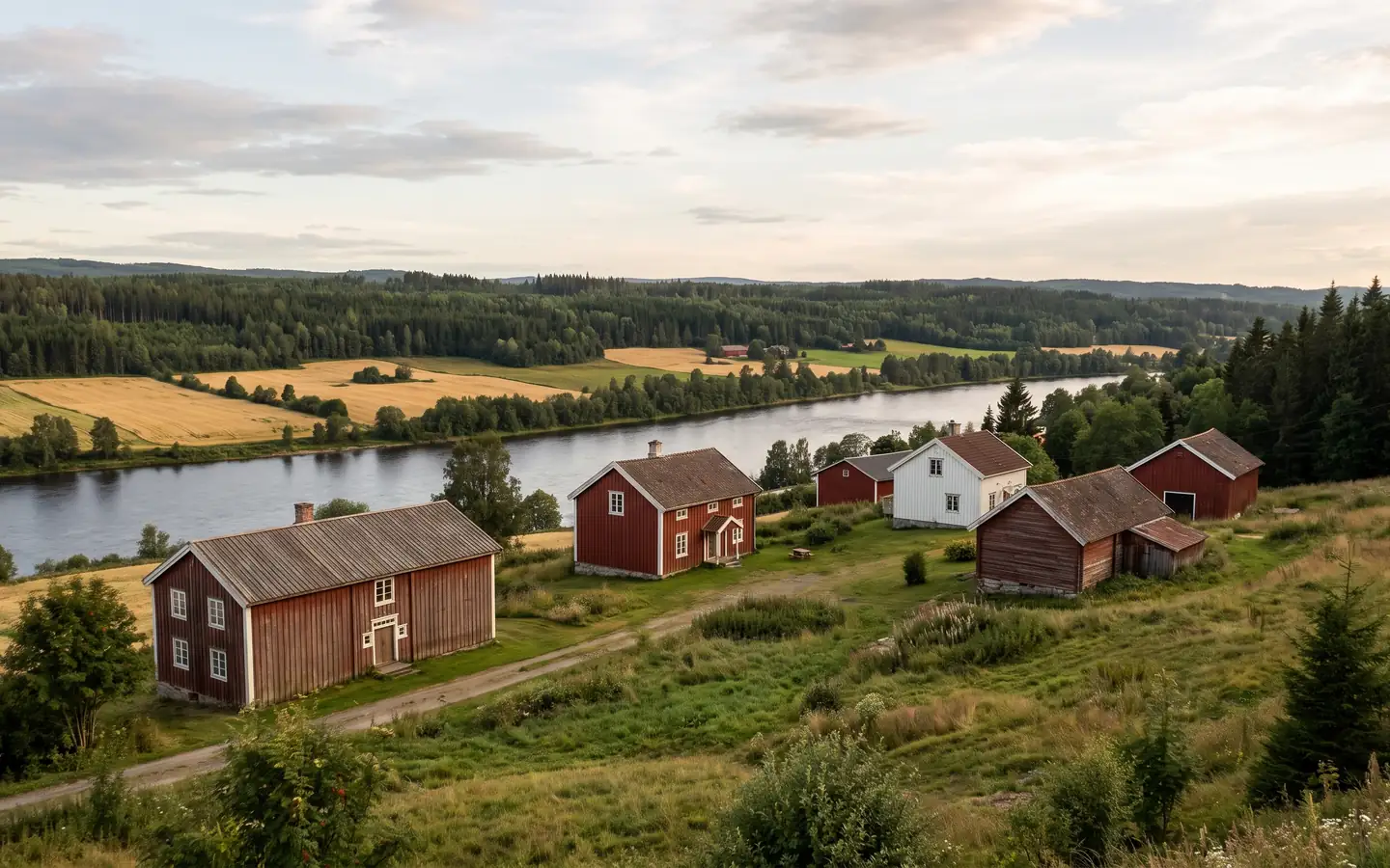 Røde og hvite trehus i en skråning over Glomma, med jorder og skog i bakgrunnen
